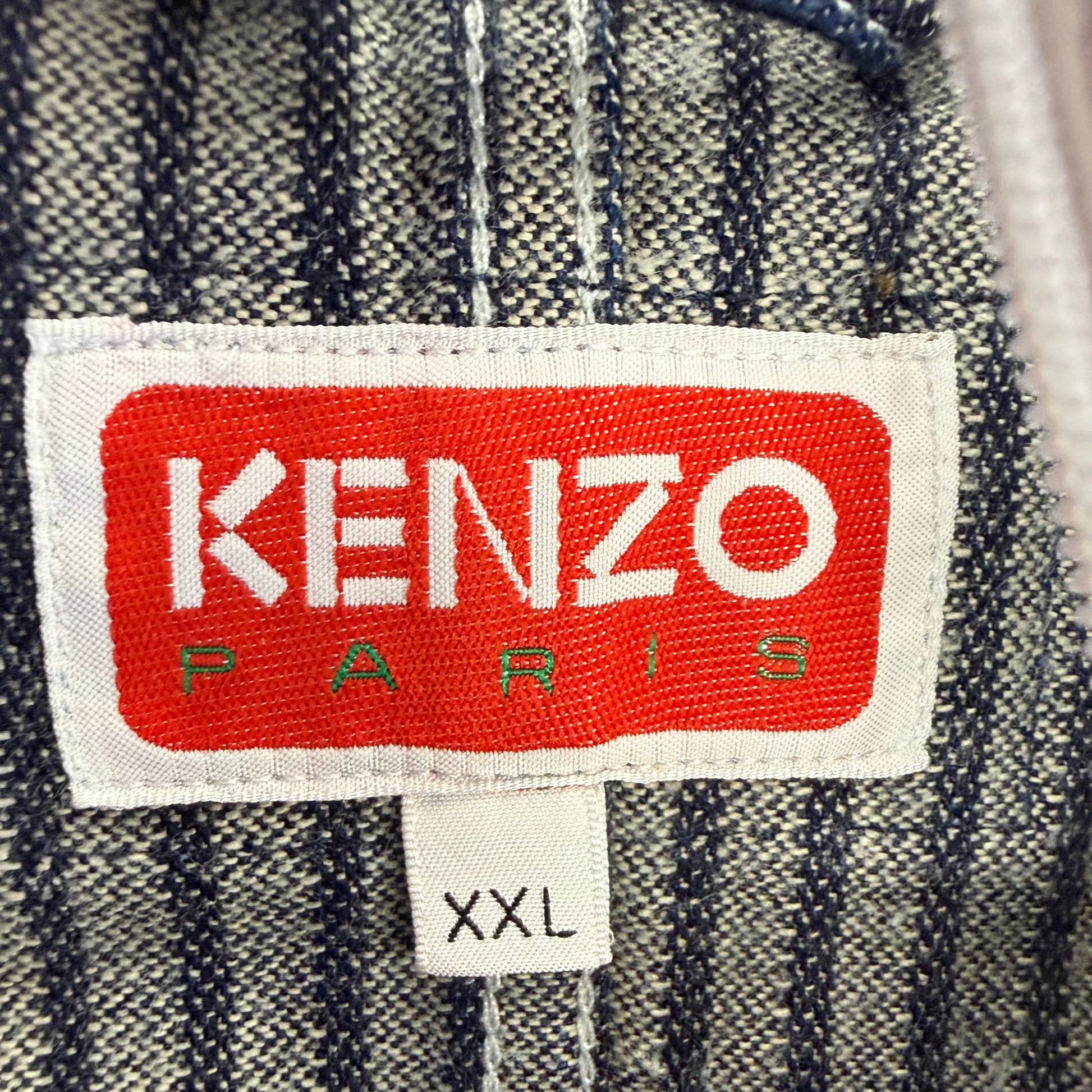 Close-up of a Kenzo Paris garment label on a gray and navy striped fabric, with a smaller size tag reading XXL below it.